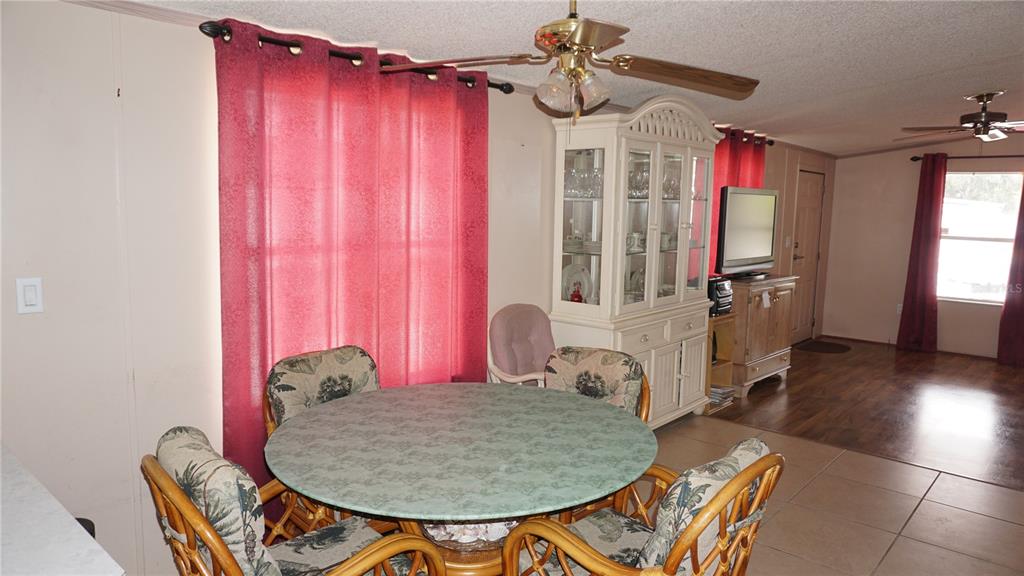A dining area features a round table with four chairs, a china cabinet, and red curtains — 12023 LONGHORN DRIVE, HUDSON, FL