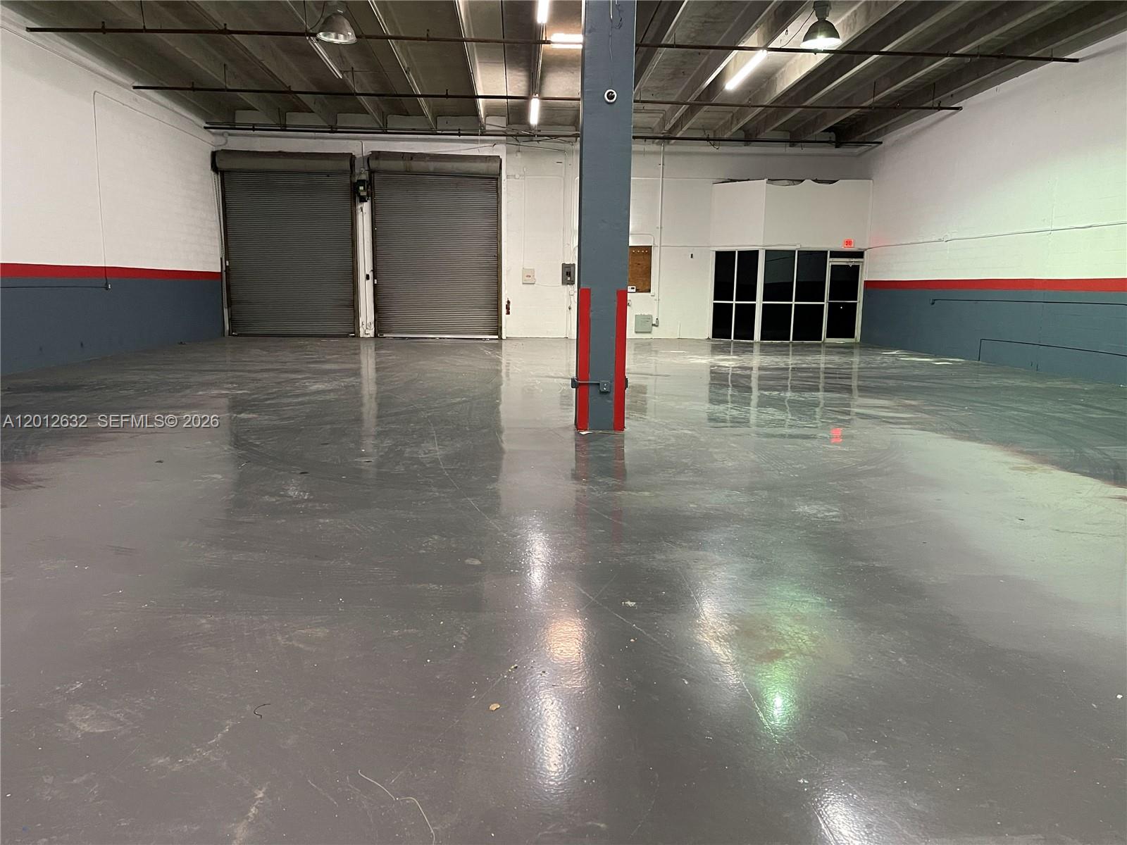 An empty warehouse space features a polished concrete floor, two roll-up doors, and a support pillar — 3004 NW 79th Ave # 3004, Doral FL 33122, DORAL, FL