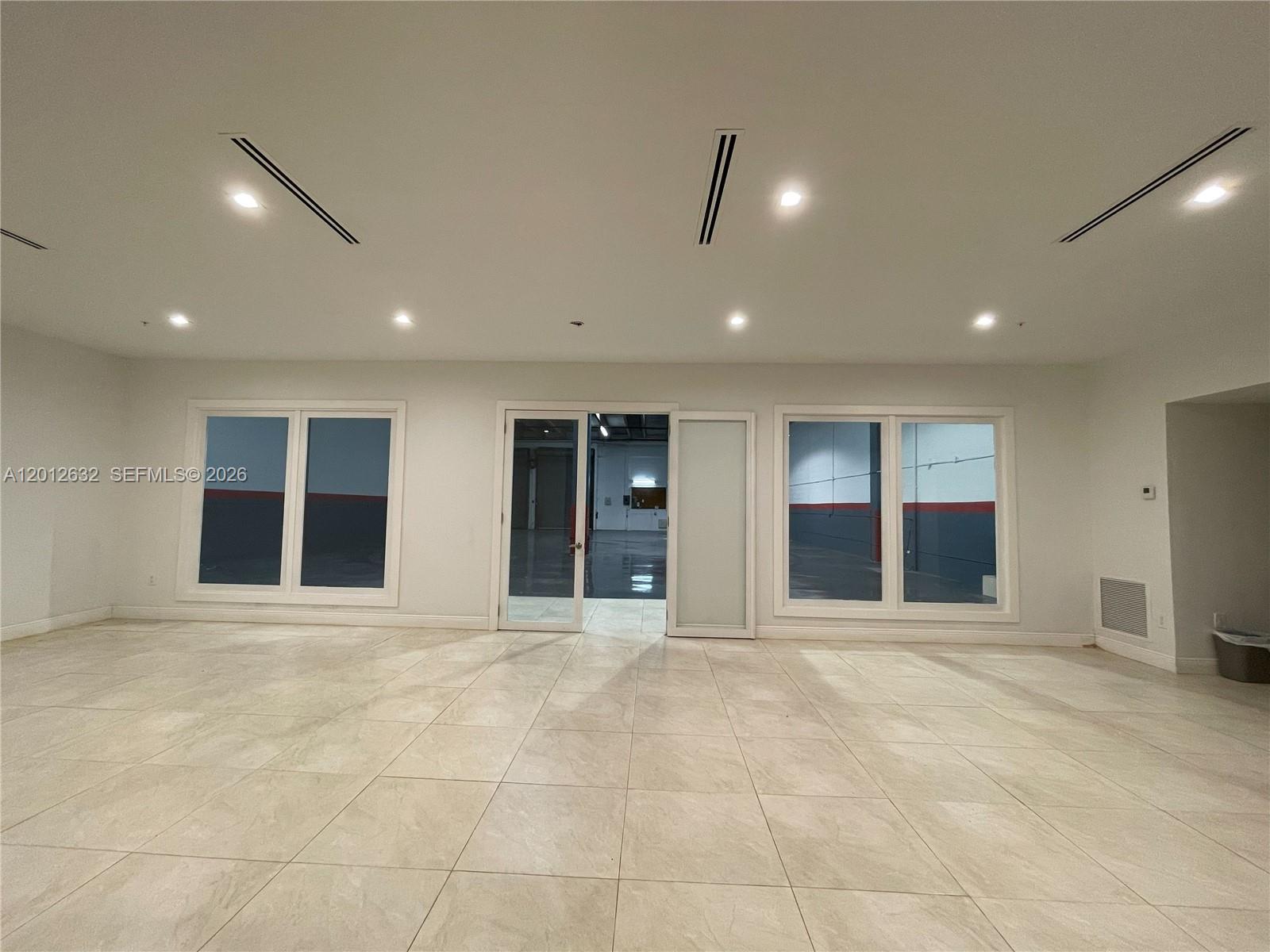 A bright, empty room features light-colored tile flooring, recessed lighting, and a central glass doorway — 3004 NW 79th Ave # 3004, Doral FL 33122, DORAL, FL