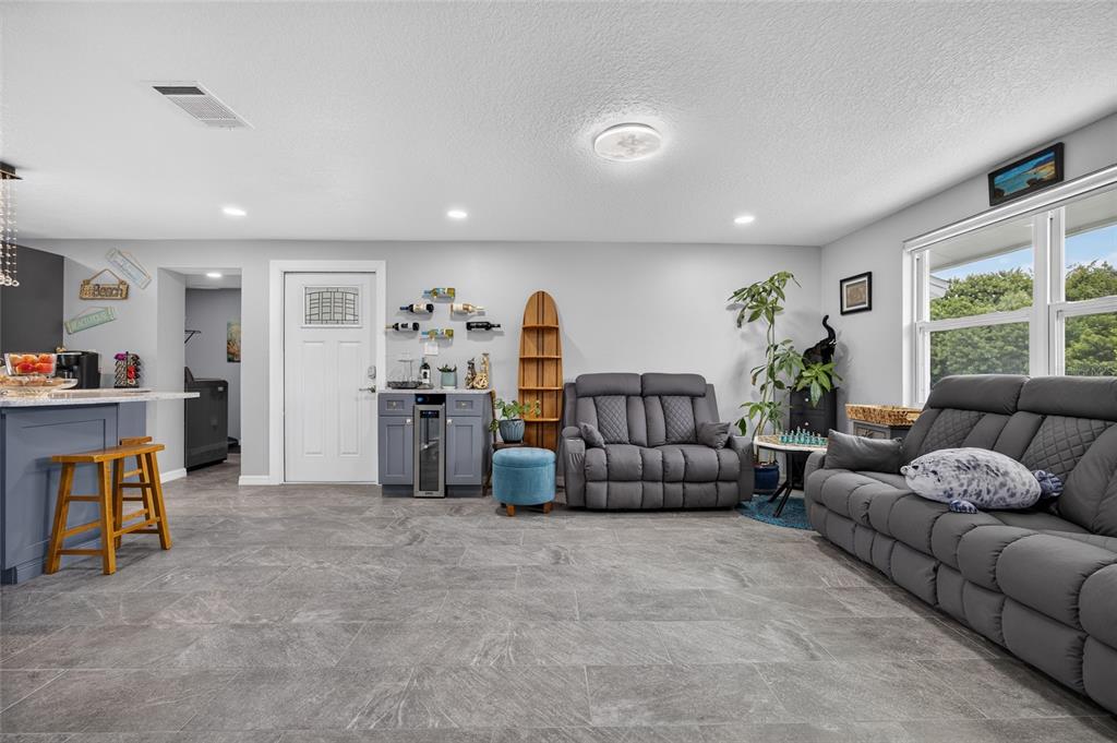 A living room features gray tile flooring, two gray reclining sofas, and a small bar area — 3165 ROCK CREEK DRIVE, PORT CHARLOTTE, FL