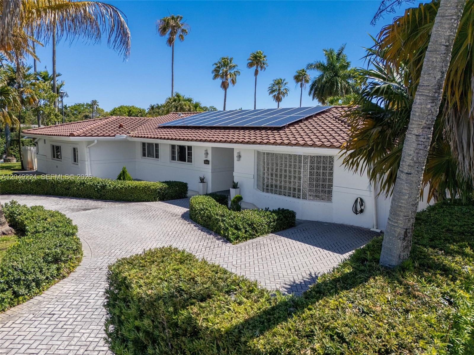 A white house with a tile roof, solar panels, and a paved driveway surrounded by landscaping — 20235 Highland Lakes Blvd, Miami FL 33179, MIAMI, FL