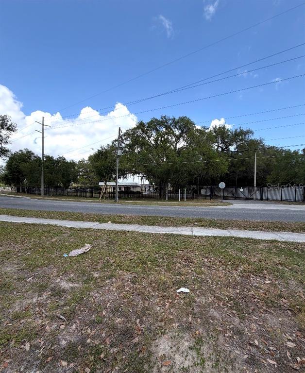A view of a grassy lot with a fence, trees, and a building in the background — N OAKLAND STREET, LEESBURG, FL