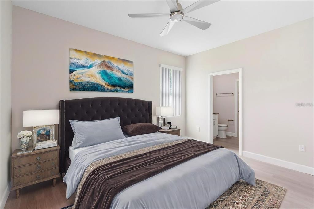 A bedroom features a tufted headboard, a ceiling fan, and an attached bathroom doorway — 1201 W 9TH STREET, SANFORD, FL