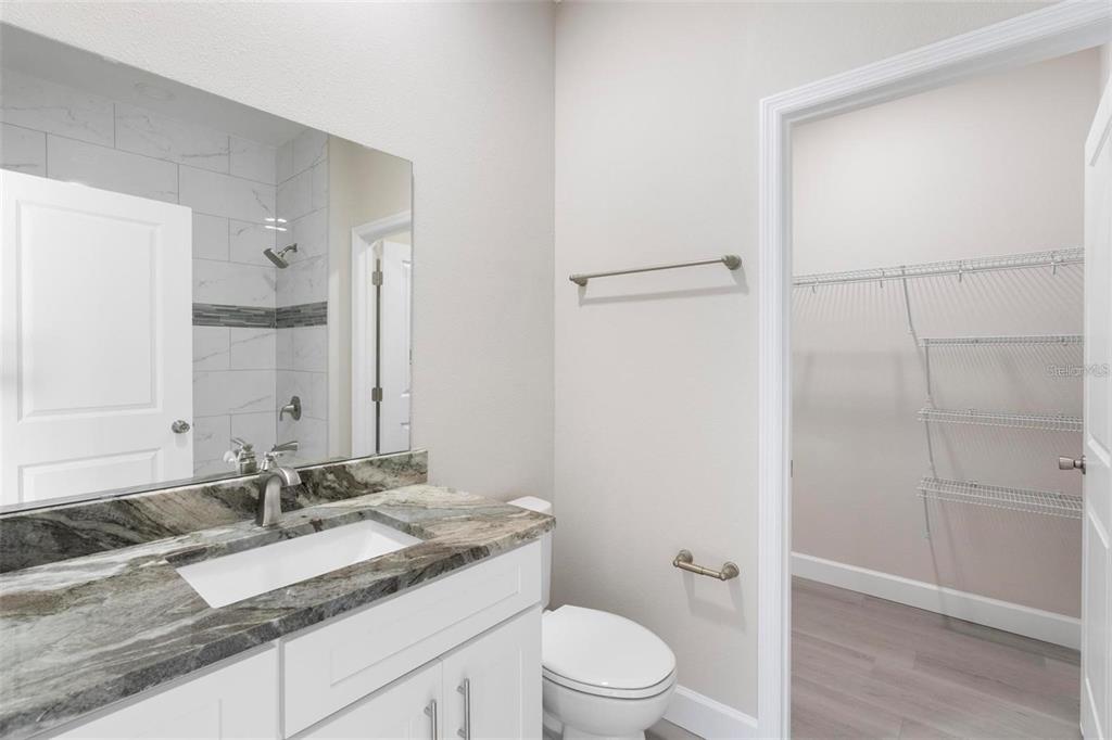 A bathroom features a stone vanity countertop, white cabinetry, a mirror, and an adjacent walk-in closet — 1201 W 9TH STREET, SANFORD, FL
