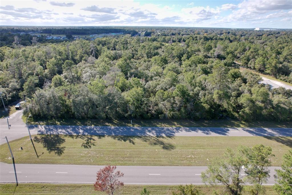 An aerial view shows a wooded lot bordering a paved road with a grassy median — MARION OAKS BOULEVARD, OCALA, FL