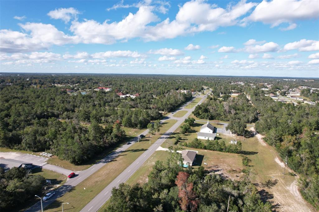 An aerial view shows a divided highway running through a wooded area with several buildings — MARION OAKS BOULEVARD, OCALA, FL