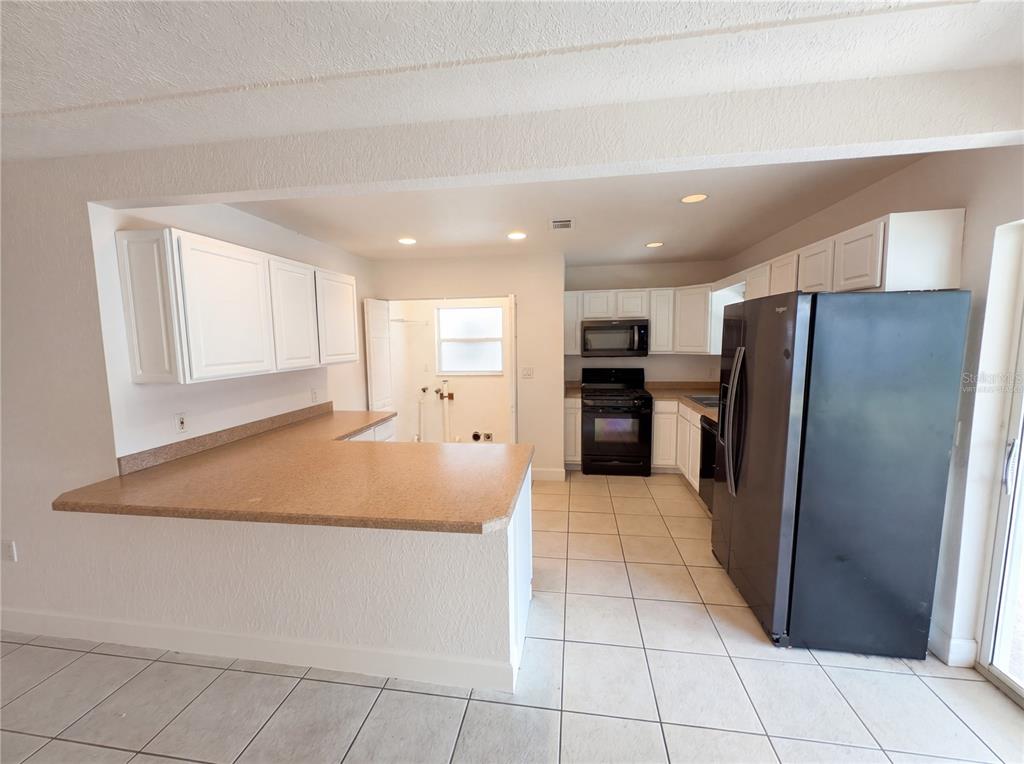 A kitchen features white cabinets, a tan countertop, black appliances, and light-colored floor tiles — 804 HAMPTON WAY, MERRITT ISLAND, FL