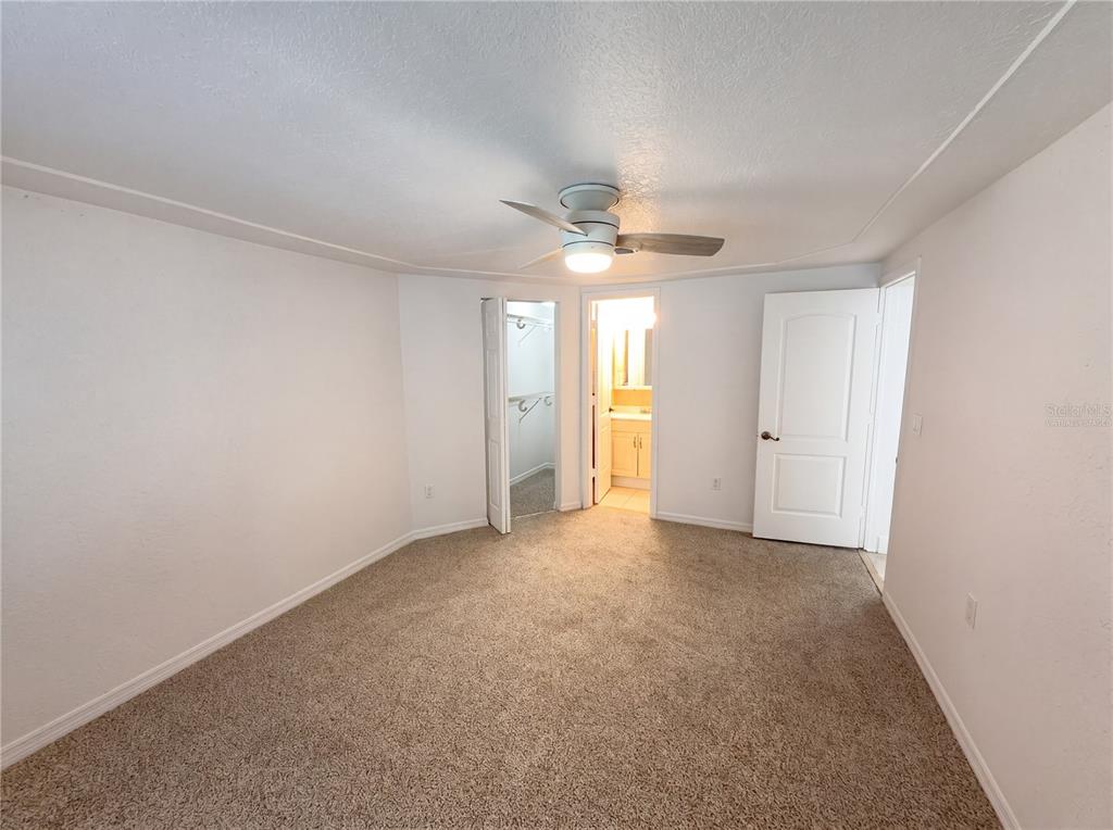 A bedroom with beige carpet, a ceiling fan, a closet, and an attached bathroom — 804 HAMPTON WAY, MERRITT ISLAND, FL