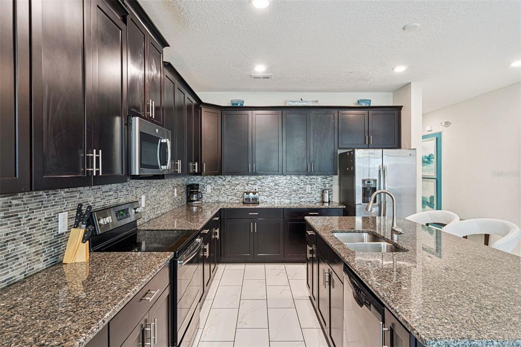 A kitchen features dark wood cabinets, granite countertops, a tiled backsplash, and stainless steel appliances — 1580 TEMPO LANE, DAVENPORT, FL