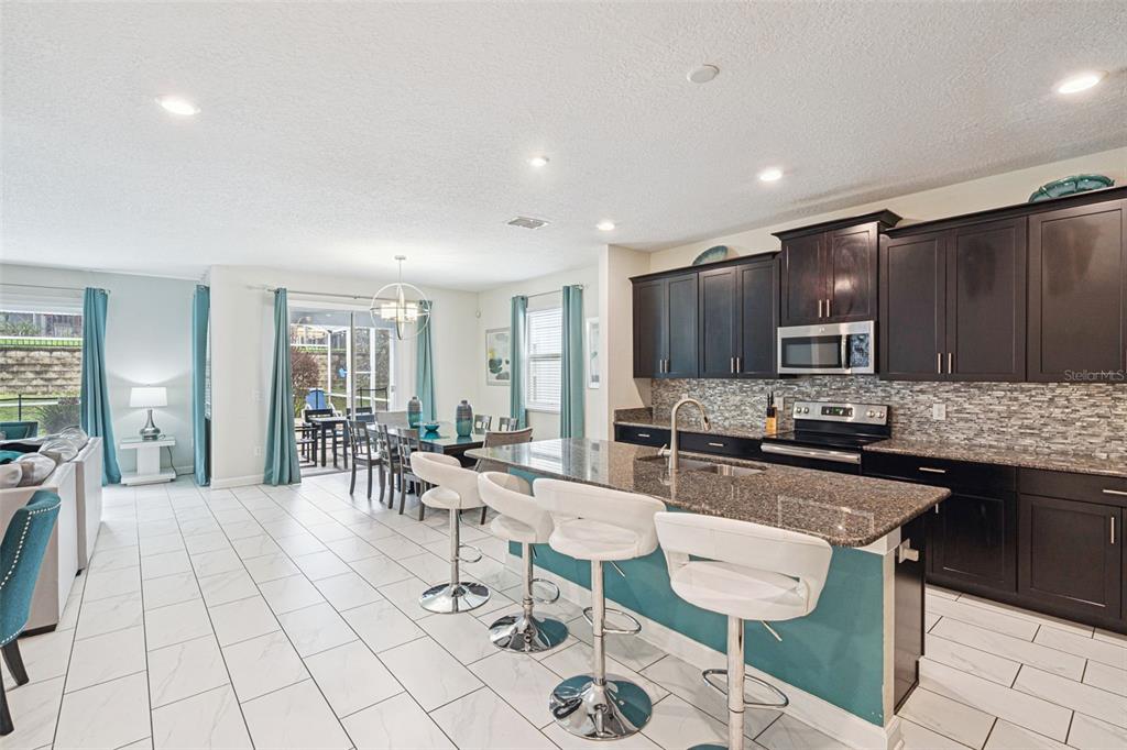 A kitchen with dark cabinets and a granite island overlooks a dining area and patio — 1580 TEMPO LANE, DAVENPORT, FL