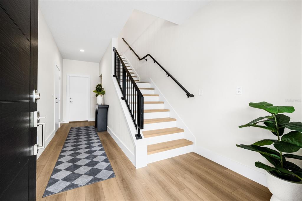 A modern entryway features light wood flooring, a staircase with black railings, and a checkered runner — 8627 5TH STREET N, ST PETERSBURG, FL