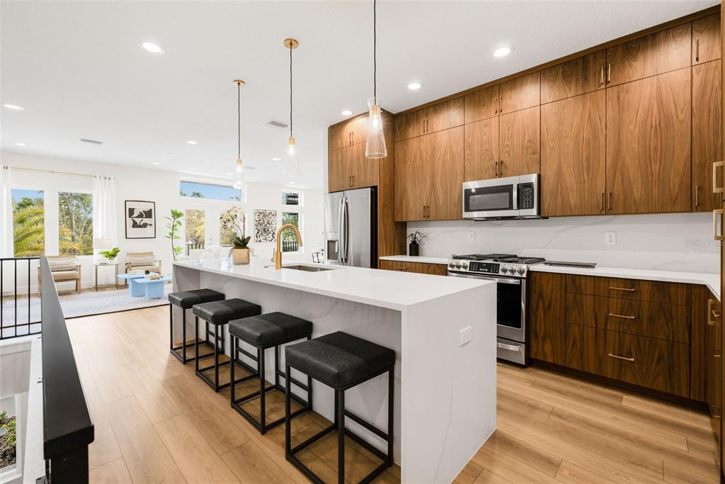 A modern kitchen features wood cabinets, a white waterfall island with stools, and stainless appliances — 8627 5TH STREET N, ST PETERSBURG, FL