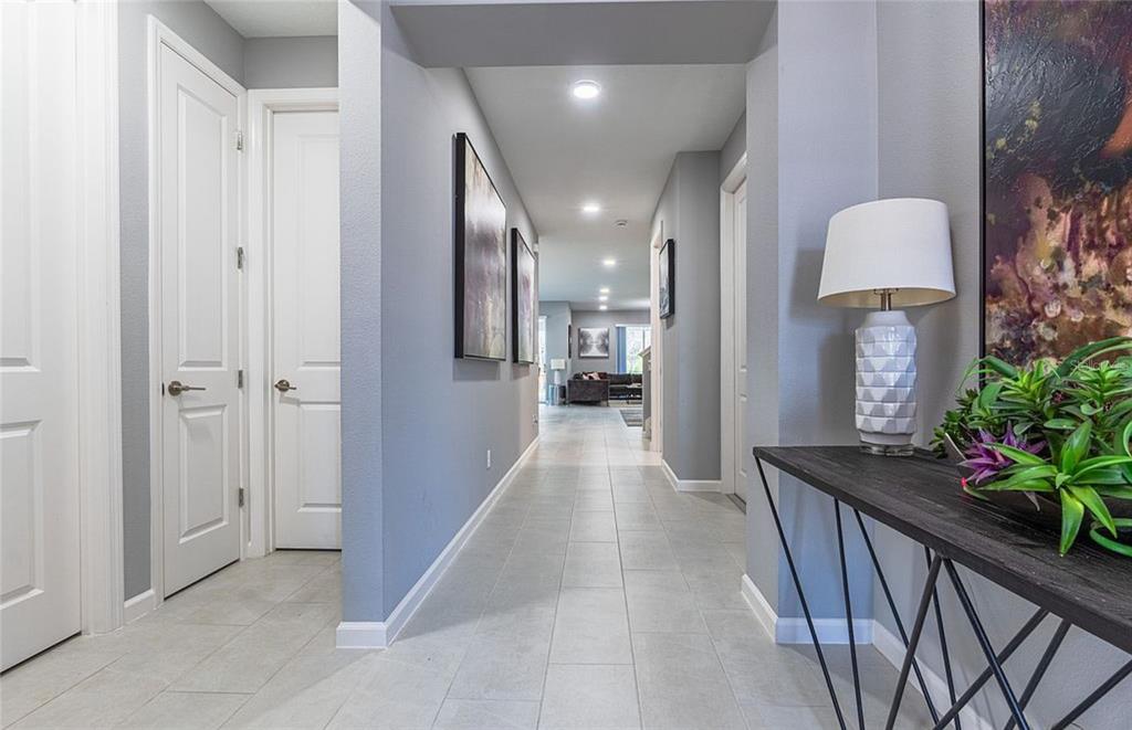 A hallway with light gray tile flooring leads toward a living area with white doors — 5055 SHADY PINES DR, ST CLOUD, FL
