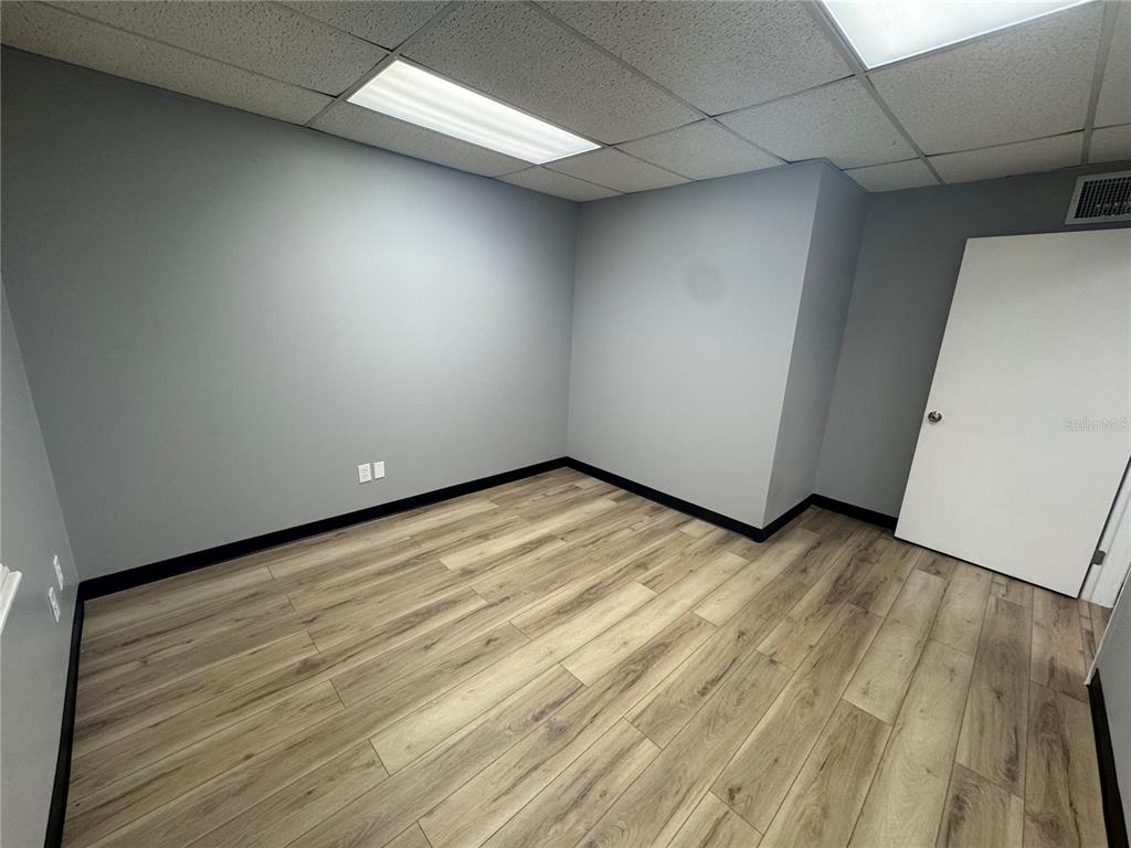 An empty office room features gray walls, wood-look flooring, a drop ceiling, and a white door — 550 N BALMORAL CIRCLE UNIT 108/109, JACKSONVILLE, FL
