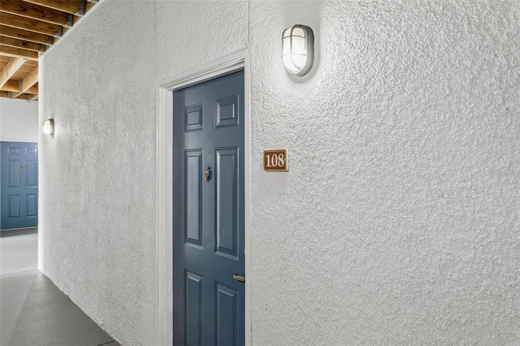 A blue door with the number 108 is set in a white textured exterior wall — 1450 VILLA CAPRI CIRCLE UNIT 108, ODESSA, FL