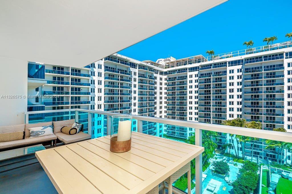 A balcony with outdoor seating and a table overlooks a large, multi-story apartment complex — 2301 Collins Ave # 1117, Miami Beach FL 33139, MIAMI BEACH, FL