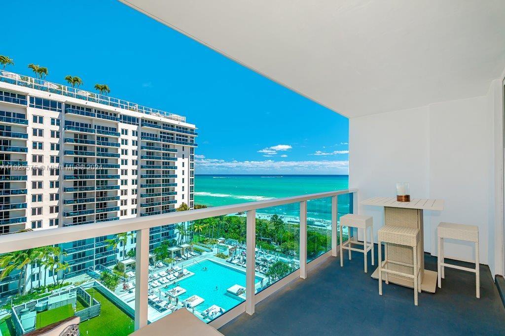 A balcony with a small table and chairs overlooks a swimming pool and the ocean — 2301 Collins Ave # 1117, Miami Beach FL 33139, MIAMI BEACH, FL