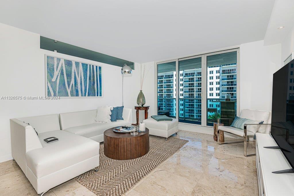 A modern living room features a white sectional sofa, a round wooden coffee table, and balcony views — 2301 Collins Ave # 1117, Miami Beach FL 33139, MIAMI BEACH, FL