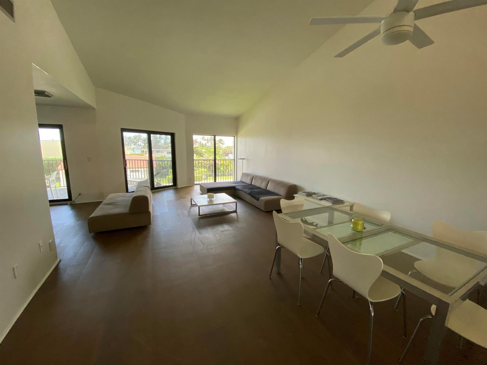 A spacious living and dining area features dark wood floors, white walls, and glass doors — 5801 N Ocean Boulevard # 208, Ocean Ridge FL 33435, OCEAN RIDGE, FL