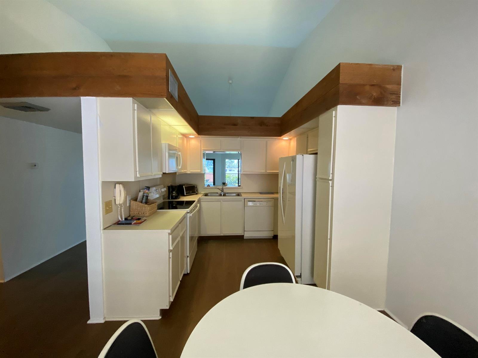 A kitchen features white cabinetry, wood-trimmed soffits, and a vaulted ceiling above a dining area — 5801 N Ocean Boulevard # 208, Ocean Ridge FL 33435, OCEAN RIDGE, FL