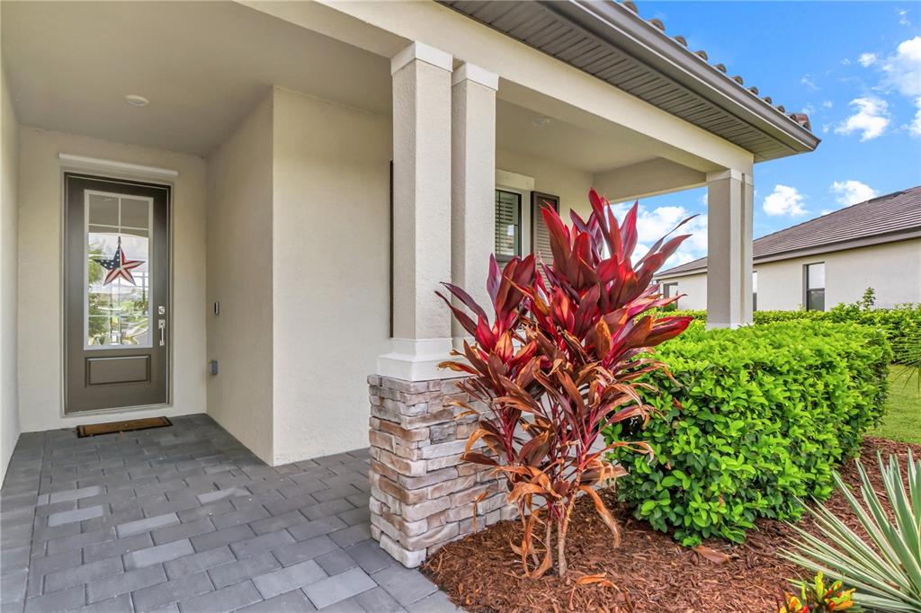 A covered front porch features a paved floor, stone-based columns, and a glass-paneled entry door — 5105 MARINA BASIN COURT, BRADENTON, FL