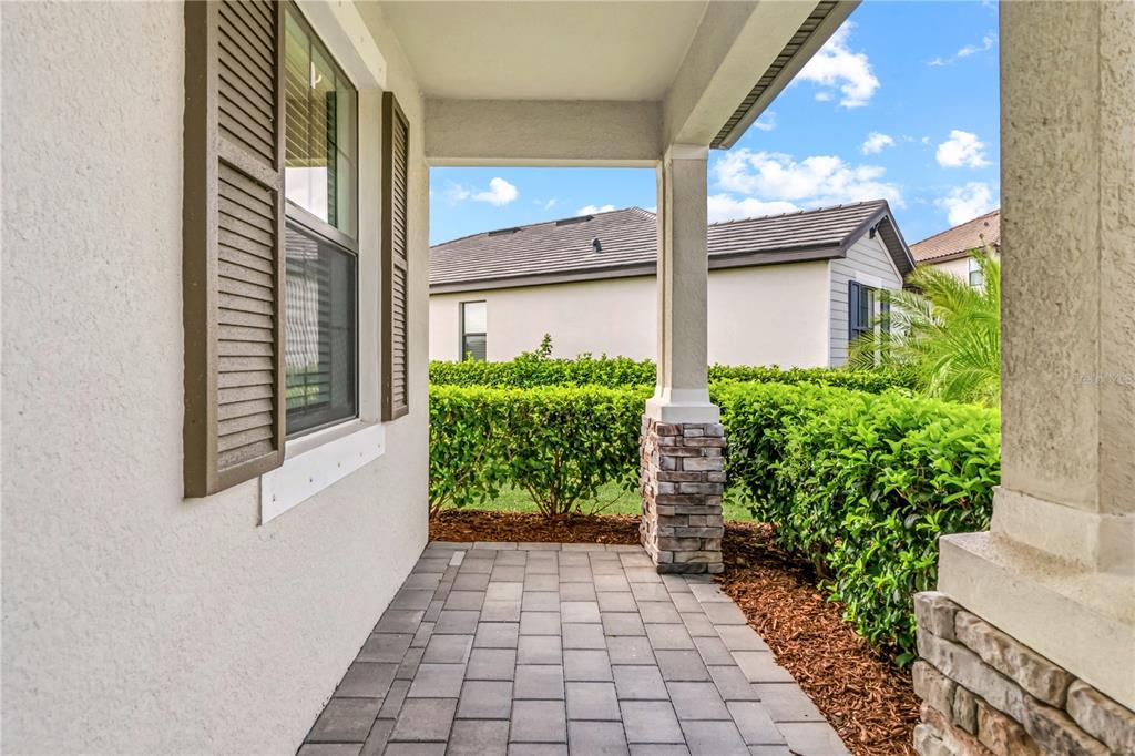 A covered porch features stone-based columns, a paver floor, and a view of neighboring hedges — 5105 MARINA BASIN COURT, BRADENTON, FL