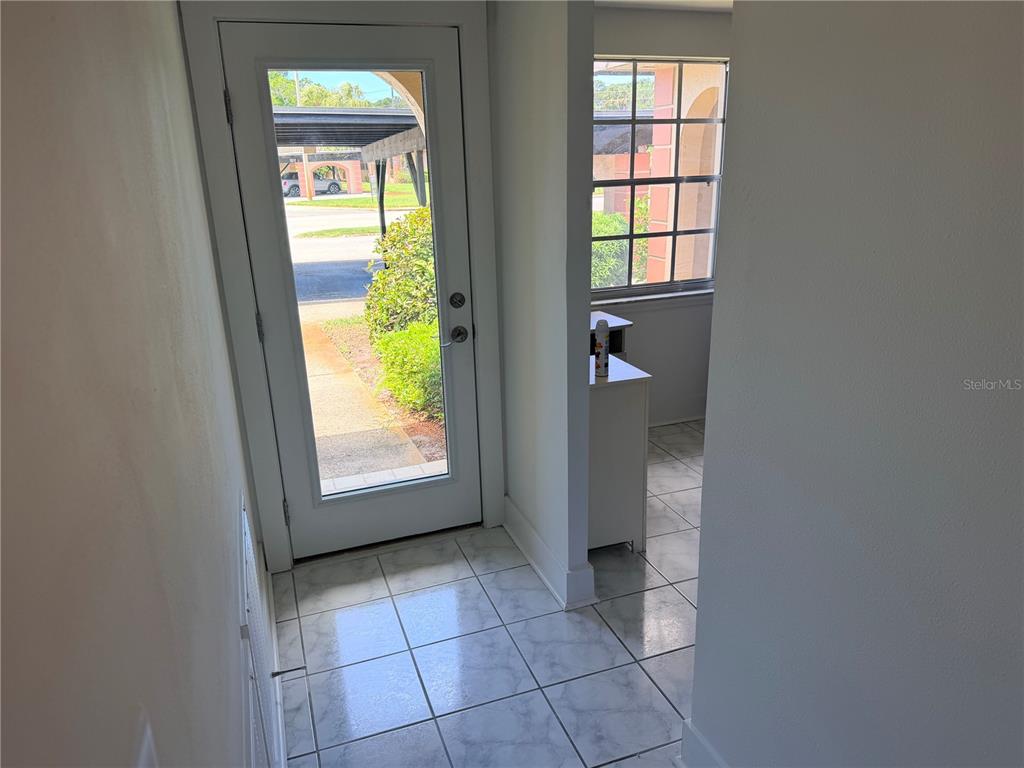 An entryway with white tile flooring, a glass-paneled front door, and a windowed wall — 4446 RUSTIC DRIVE UNIT E, NEW PORT RICHEY, FL