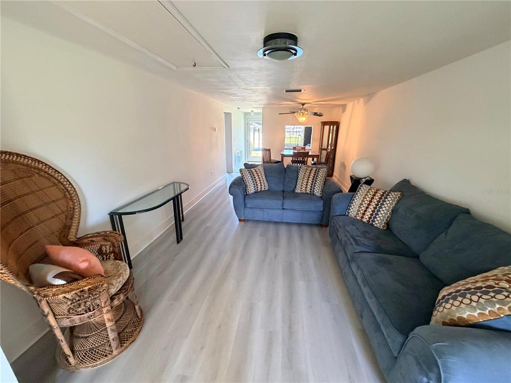 A living room features light wood-look flooring, two blue sofas, and a wicker chair — 4446 RUSTIC DRIVE UNIT E, NEW PORT RICHEY, FL