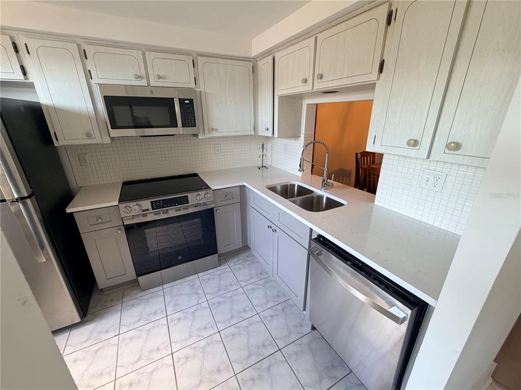 A kitchen features light-colored cabinets, stainless steel appliances, white countertops, and a tiled floor — 4446 RUSTIC DRIVE UNIT E, NEW PORT RICHEY, FL