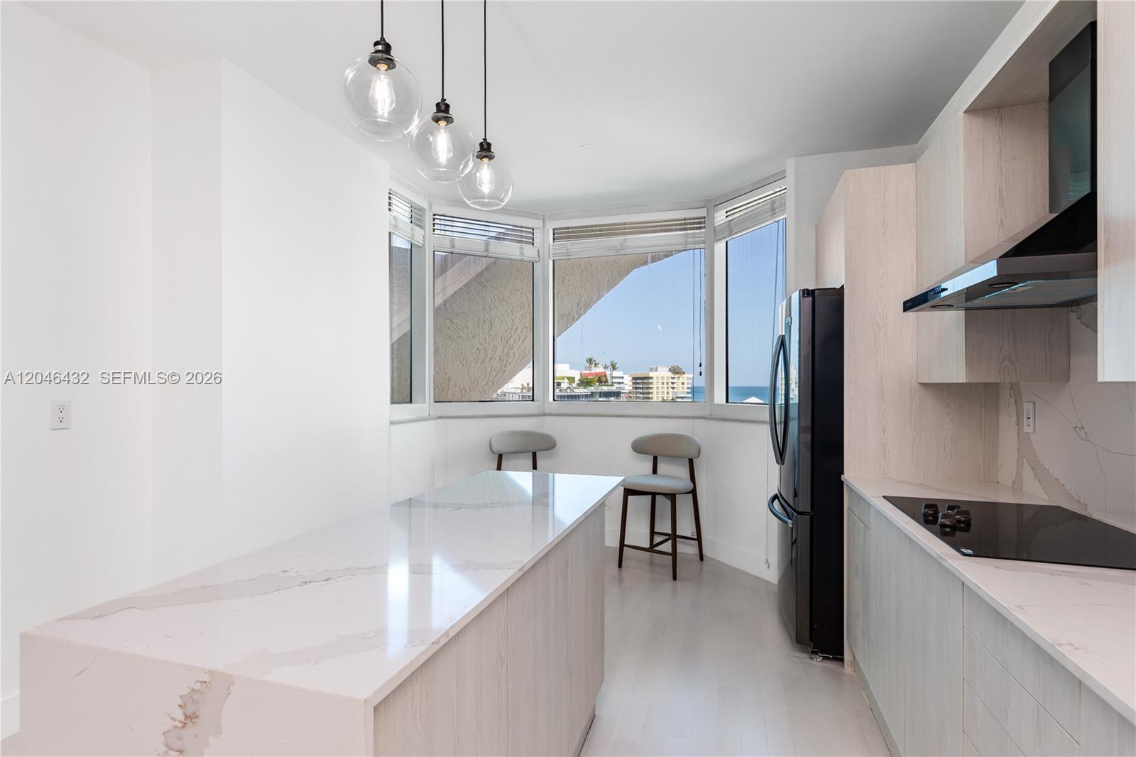 A modern kitchen features a marble-topped island, light wood cabinetry, and a windowed breakfast nook — 300 S Pointe Dr # 907, Miami Beach FL 33139, MIAMI BEACH, FL
