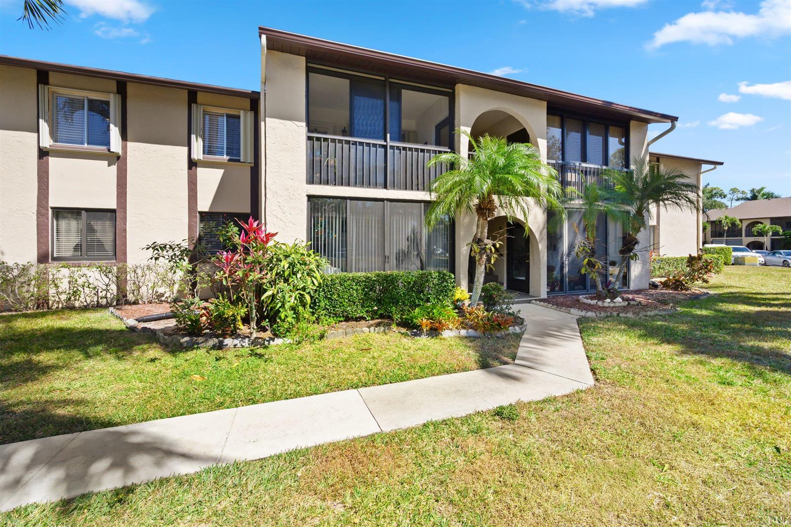 A two-story apartment building features beige stucco walls, screened balconies, and a concrete walkway — 431 Pine Glen Lane # 2, FL 33463, FL