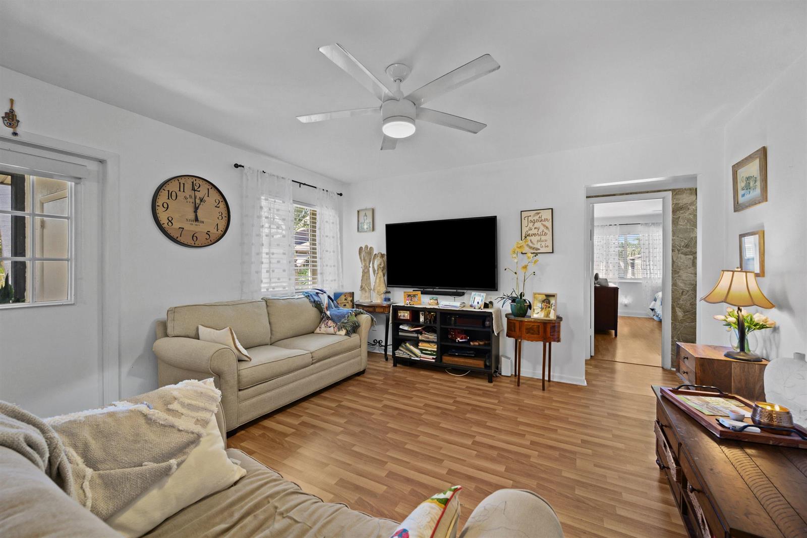 A living room with light wood floors, a beige sofa, a television, and a ceiling fan — 431 Pine Glen Lane # 2, FL 33463, FL