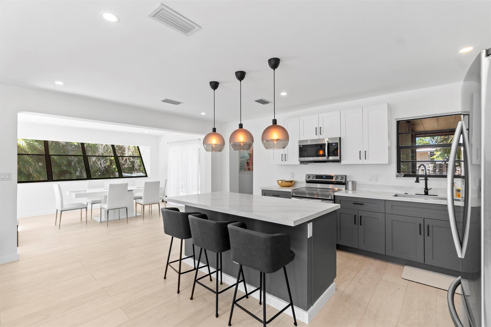 A modern kitchen features a gray island with bar stools, white upper cabinets, and light flooring — 235 NE 20th Street, Boca Raton FL 33431, BOCA RATON, FL