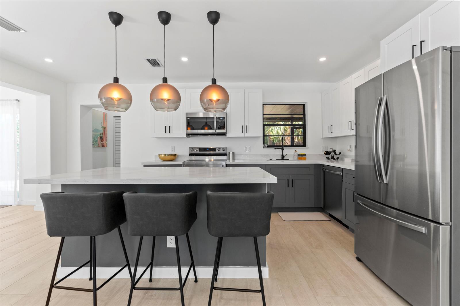 A modern kitchen features a gray island with bar stools, white cabinets, and stainless appliances — 235 NE 20th Street, Boca Raton FL 33431, BOCA RATON, FL