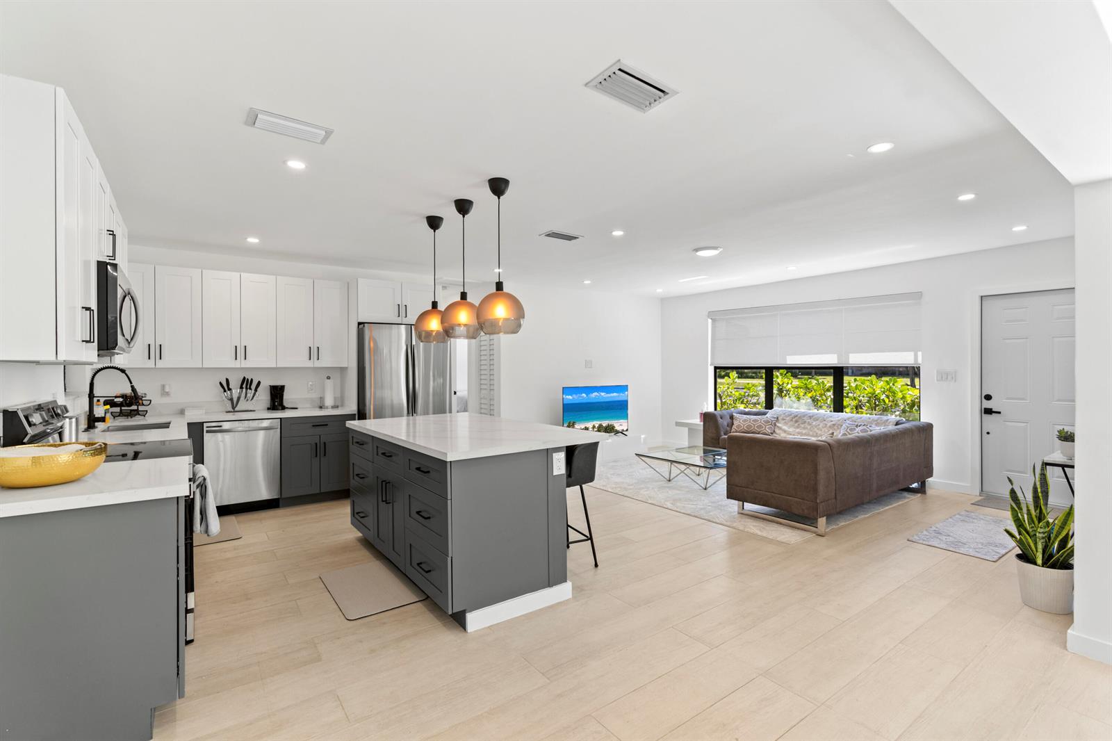 A modern open-concept kitchen and living area features white cabinets, a gray island, and wood-look flooring — 235 NE 20th Street, Boca Raton FL 33431, BOCA RATON, FL