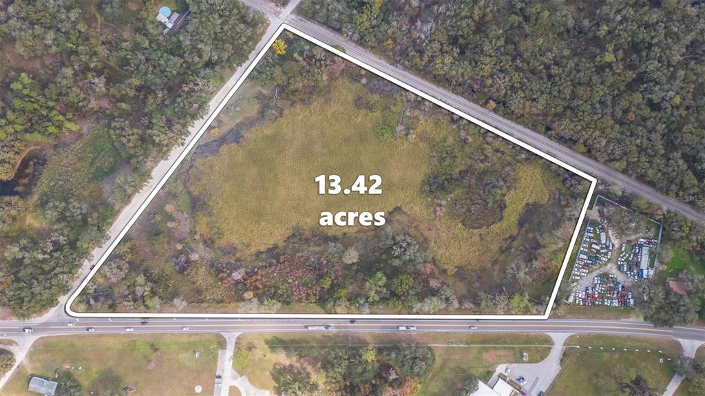 An aerial view shows a triangular 13.42-acre plot of land bordered by roads and trees — 2050 PAUL S BUCHMAN HIGHWAY, ZEPHYRHILLS, FL