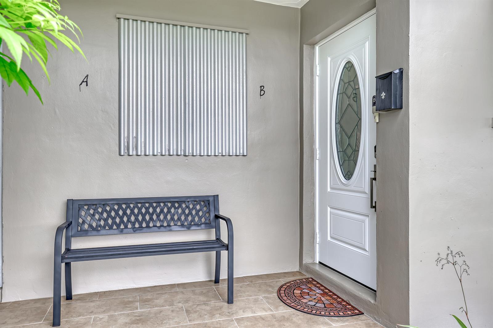 A metal bench sits on a tiled porch next to a white door with a window — 245 Main Boulevard # B, Boynton Beach FL 33435, BOYNTON BEACH, FL