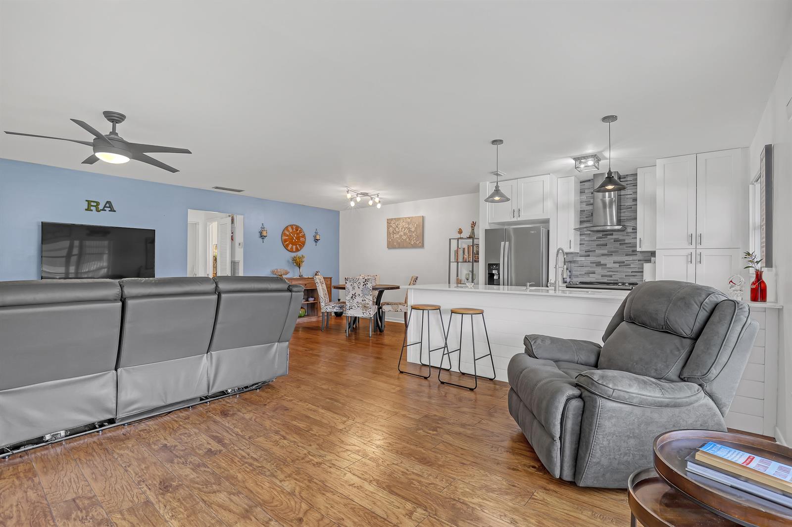An open-concept living room and kitchen feature gray furniture, wood flooring, and white cabinetry — 245 Main Boulevard # B, Boynton Beach FL 33435, BOYNTON BEACH, FL
