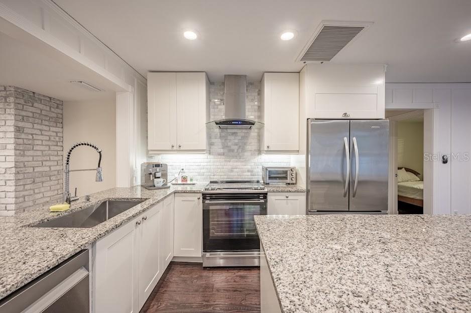 A kitchen with white cabinets, granite countertops, stainless steel appliances, and a brick accent wall — 1837 WORRINGTON STREET, SARASOTA, FL