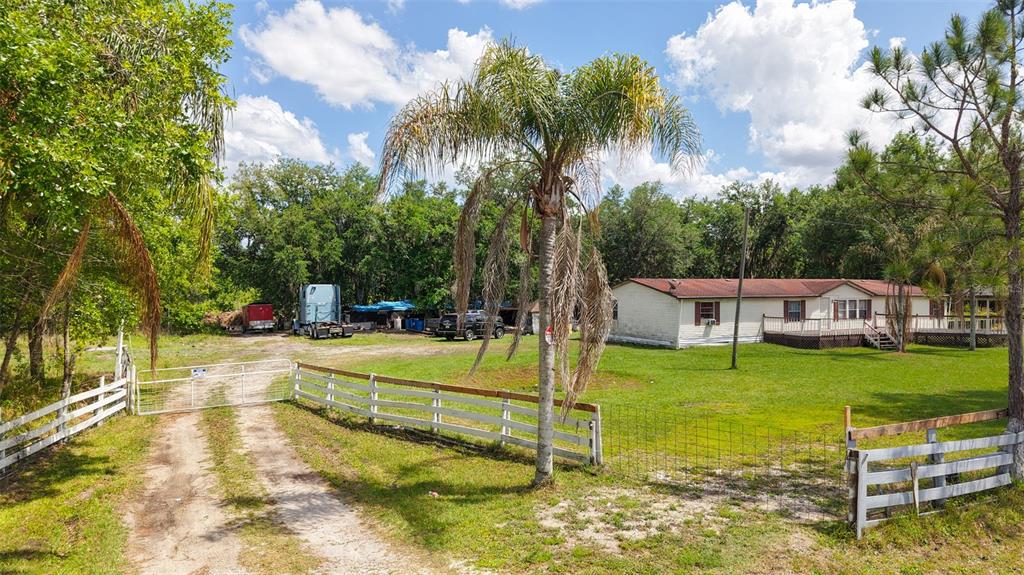 A single-story manufactured home sits on a grassy lot behind a white wooden fence — 3604 CORK ROAD, PLANT CITY, FL