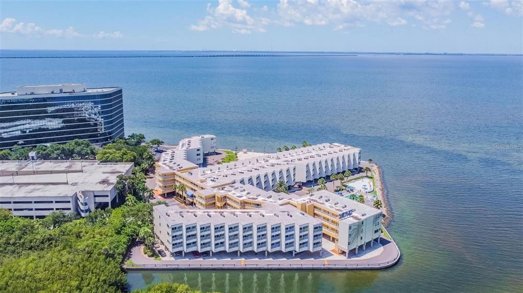 An aerial view of a multi-story waterfront apartment complex surrounded by a large body of water — 2506 N ROCKY POINT DRIVE UNIT 305, TAMPA, FL