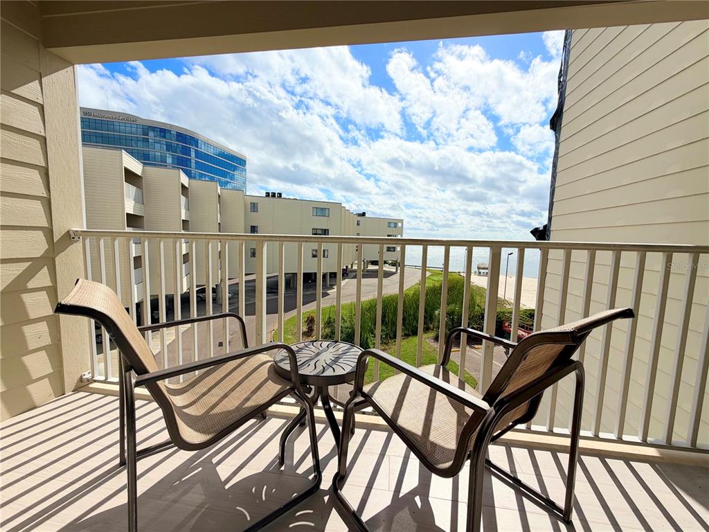 A balcony with two chairs and a small table overlooks a beach and nearby buildings — 2506 N ROCKY POINT DRIVE UNIT 305, TAMPA, FL