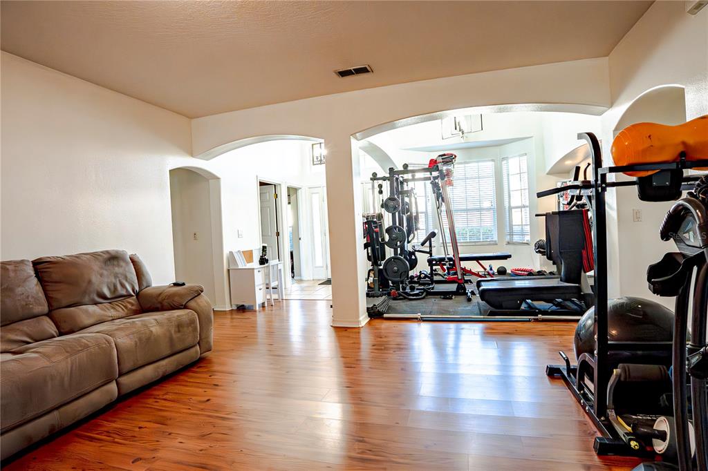 A living room with wood-look flooring features a brown sofa and an adjacent home gym — 1400 BENT OAKS BOULEVARD, DELAND, FL