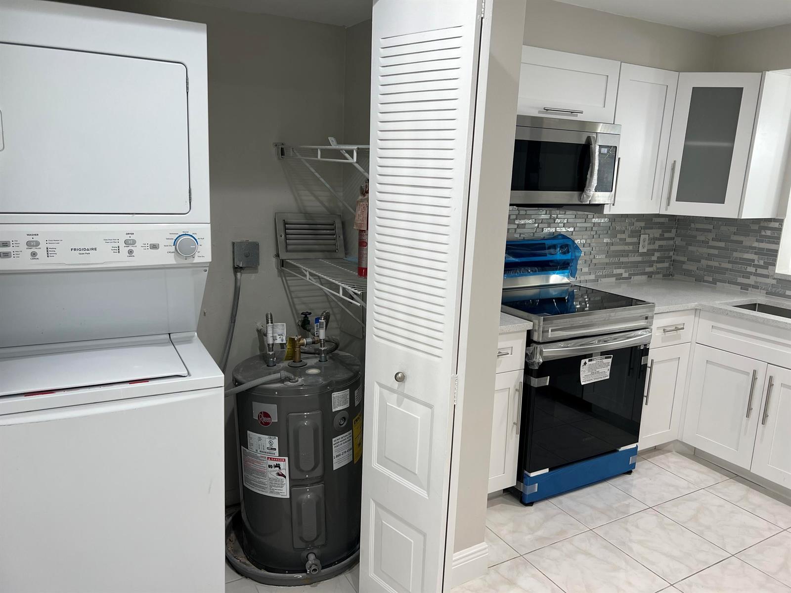A laundry closet with a water heater sits next to a kitchen with white cabinets — 24 Abbey Lane # 204, Delray Beach FL 33446, DELRAY BEACH, FL