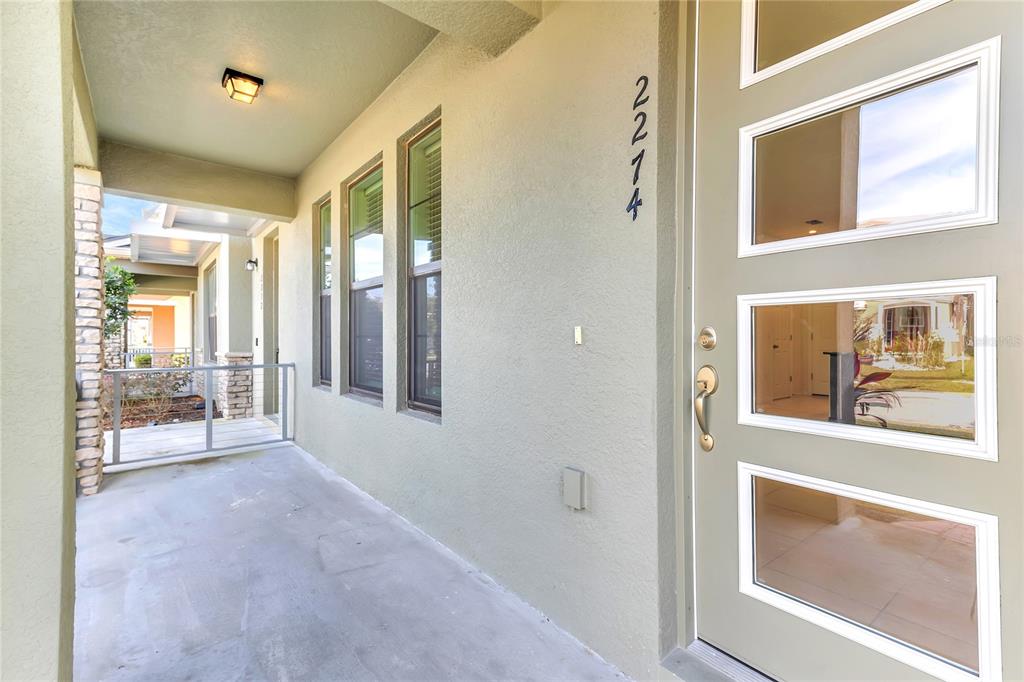 A covered entryway features a light green front door with glass panels and concrete flooring — 2274 CENTERRA LOOP, KISSIMMEE, FL
