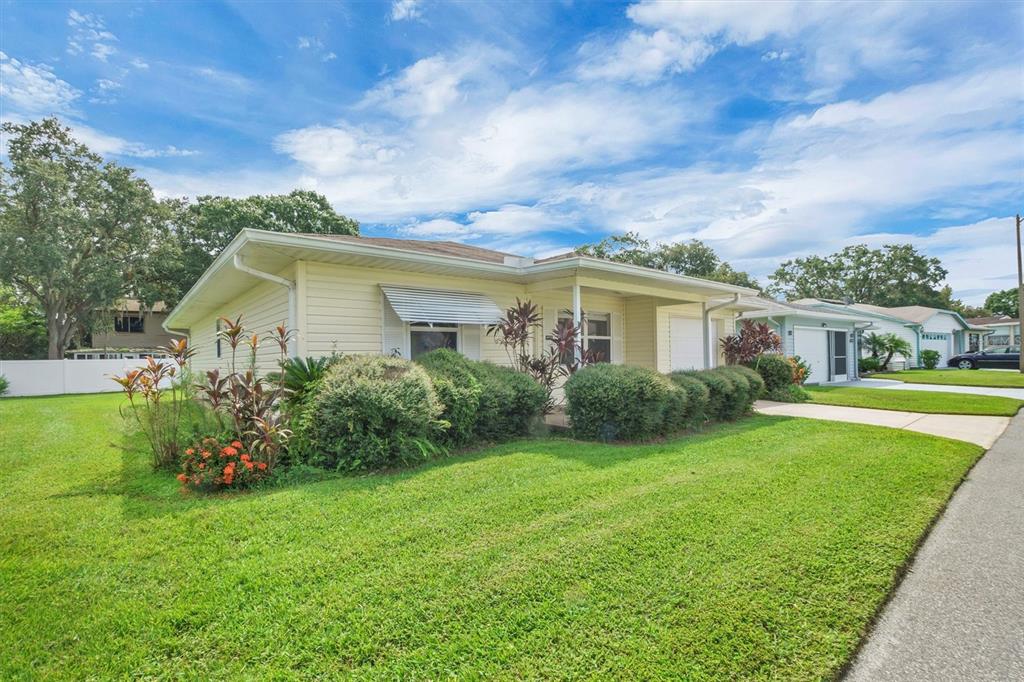 A light yellow single-story house with a front porch and landscaped bushes under a blue sky — 4938 COLONNADES CIRCLE E, LAKELAND, FL