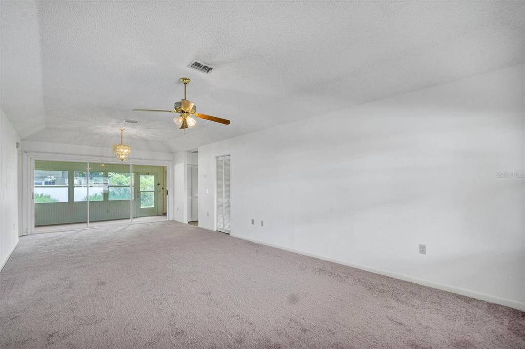 A spacious carpeted living room features a ceiling fan, a chandelier, and sliding glass doors — 4938 COLONNADES CIRCLE E, LAKELAND, FL