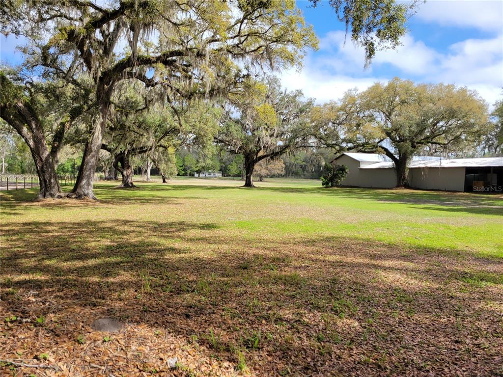 A large, grassy yard features several mature oak trees and a long metal storage building — 22397 MONDON HILL ROAD, BROOKSVILLE, FL