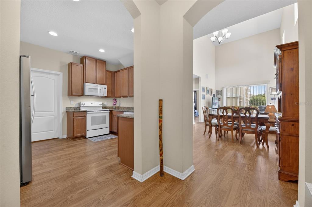 A kitchen with wood cabinets and white appliances opens into a dining area with wood floors — 2130 BROADWAY VIEW AVENUE, BRANDON, FL