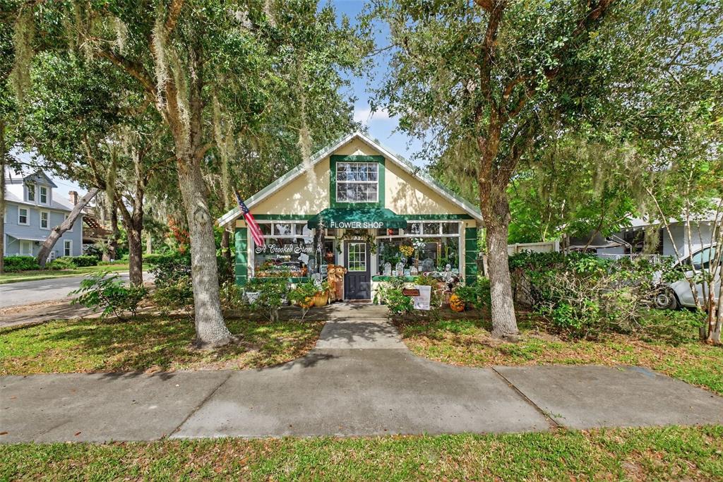 A small, yellow, single-story flower shop with a green awning sits behind two large trees — 237 E PLYMOUTH AVENUE, DELAND, FL